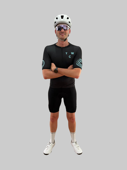 Person wearing a black cycling outfit with 'TWC' branding on a gray background