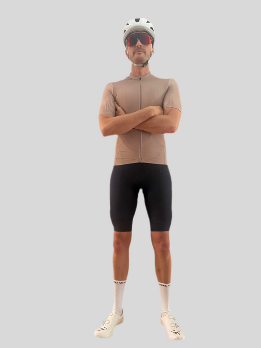 Man wearing a beige cycling jersey and black shorts with a helmet and sunglasses on a light gray background