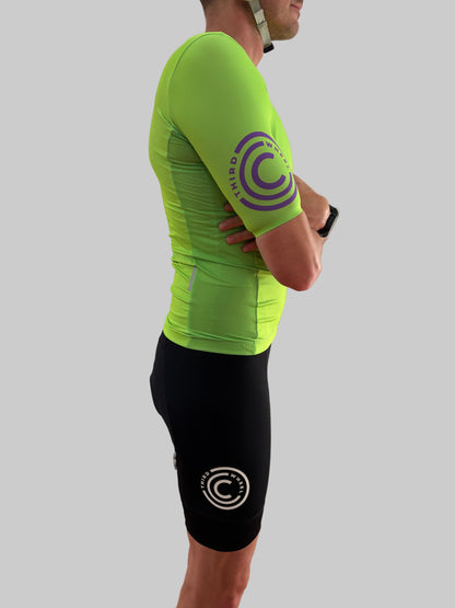 Person wearing a bright green athletic shirt and black shorts with logos on a plain background
