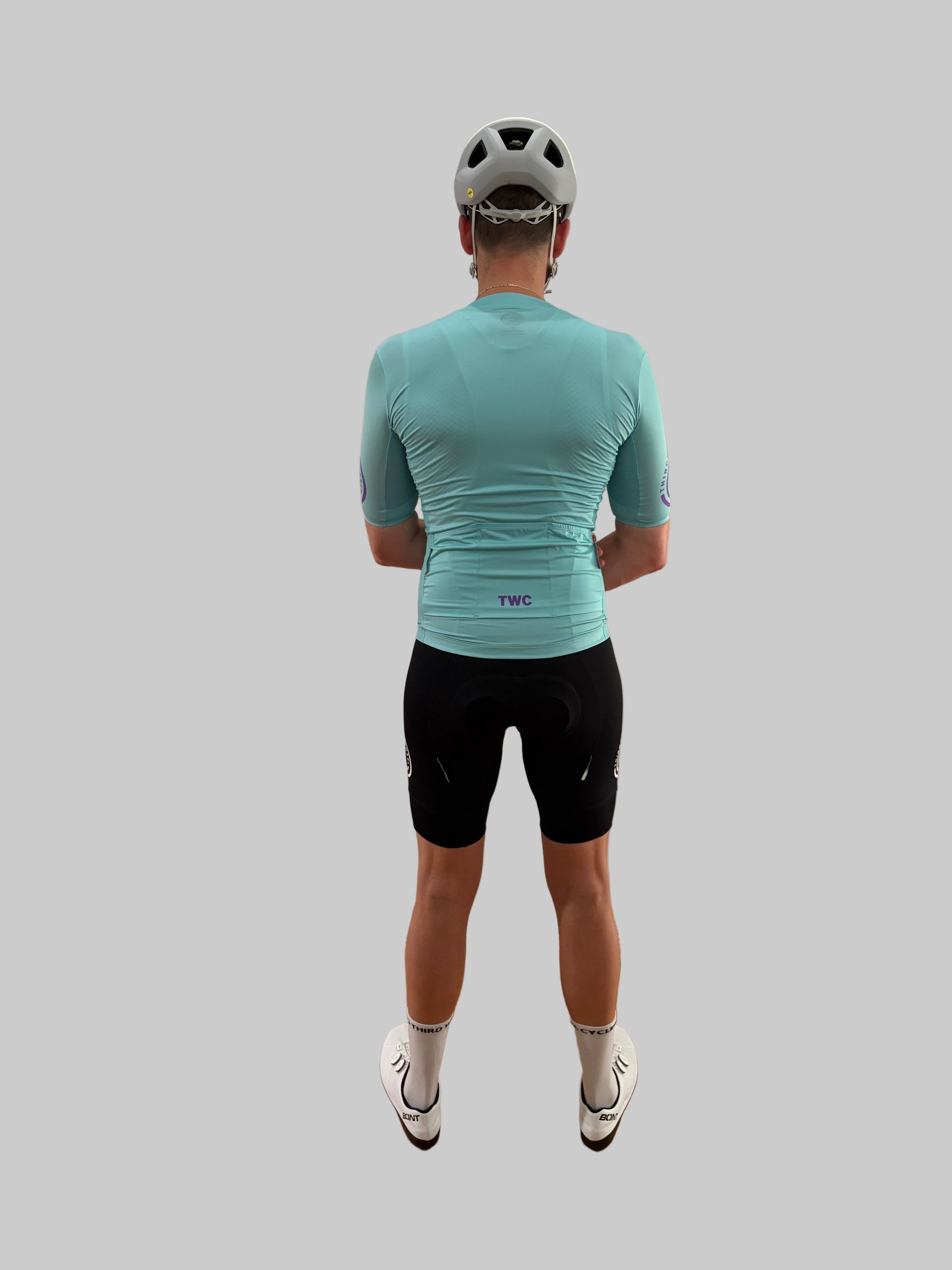Person wearing a teal cycling jersey and black shorts on a gray background