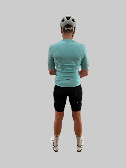 Person wearing a teal cycling jersey and black shorts on a gray background