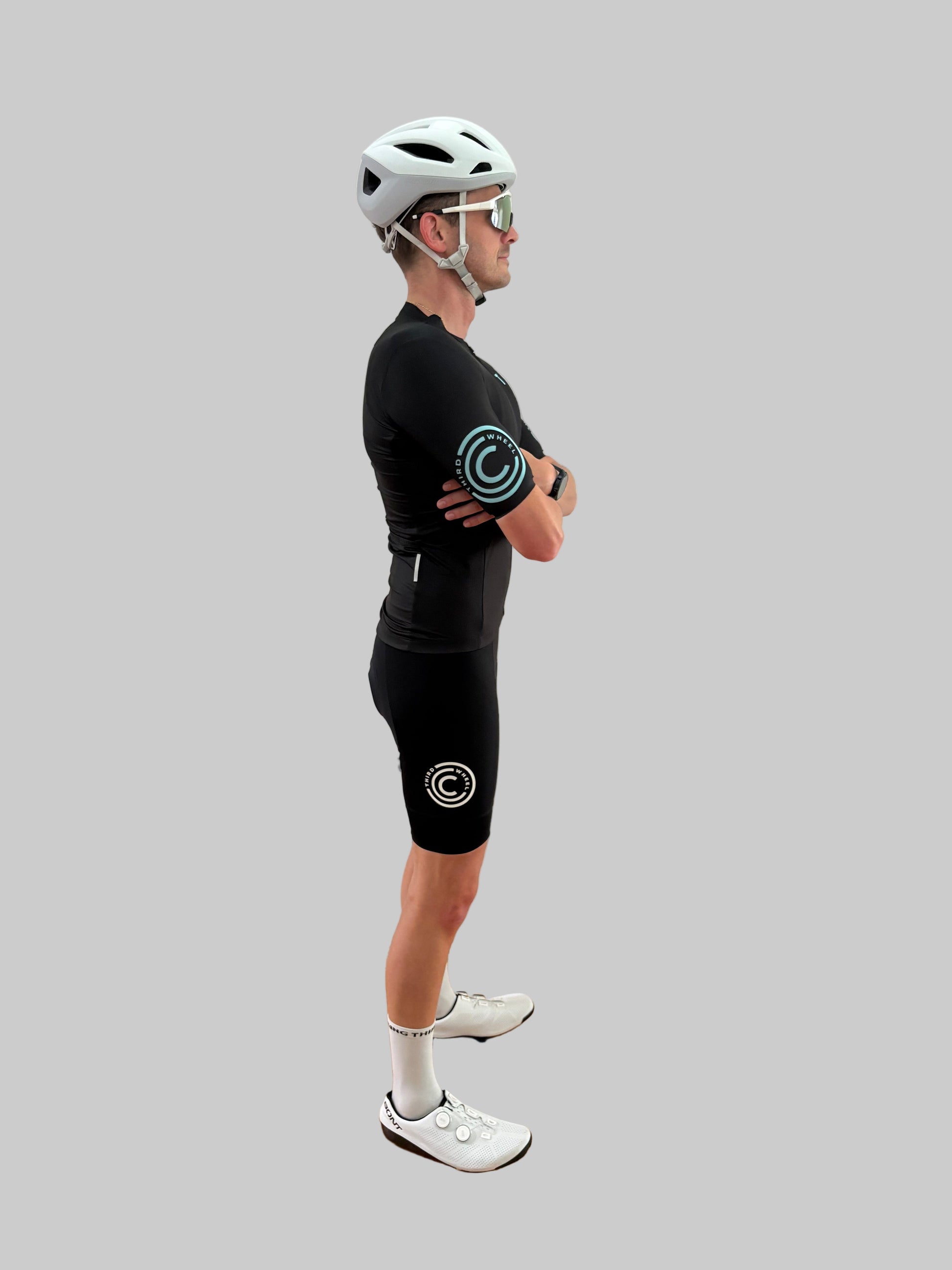 Person wearing a black cycling outfit with a helmet and sunglasses on a gray background